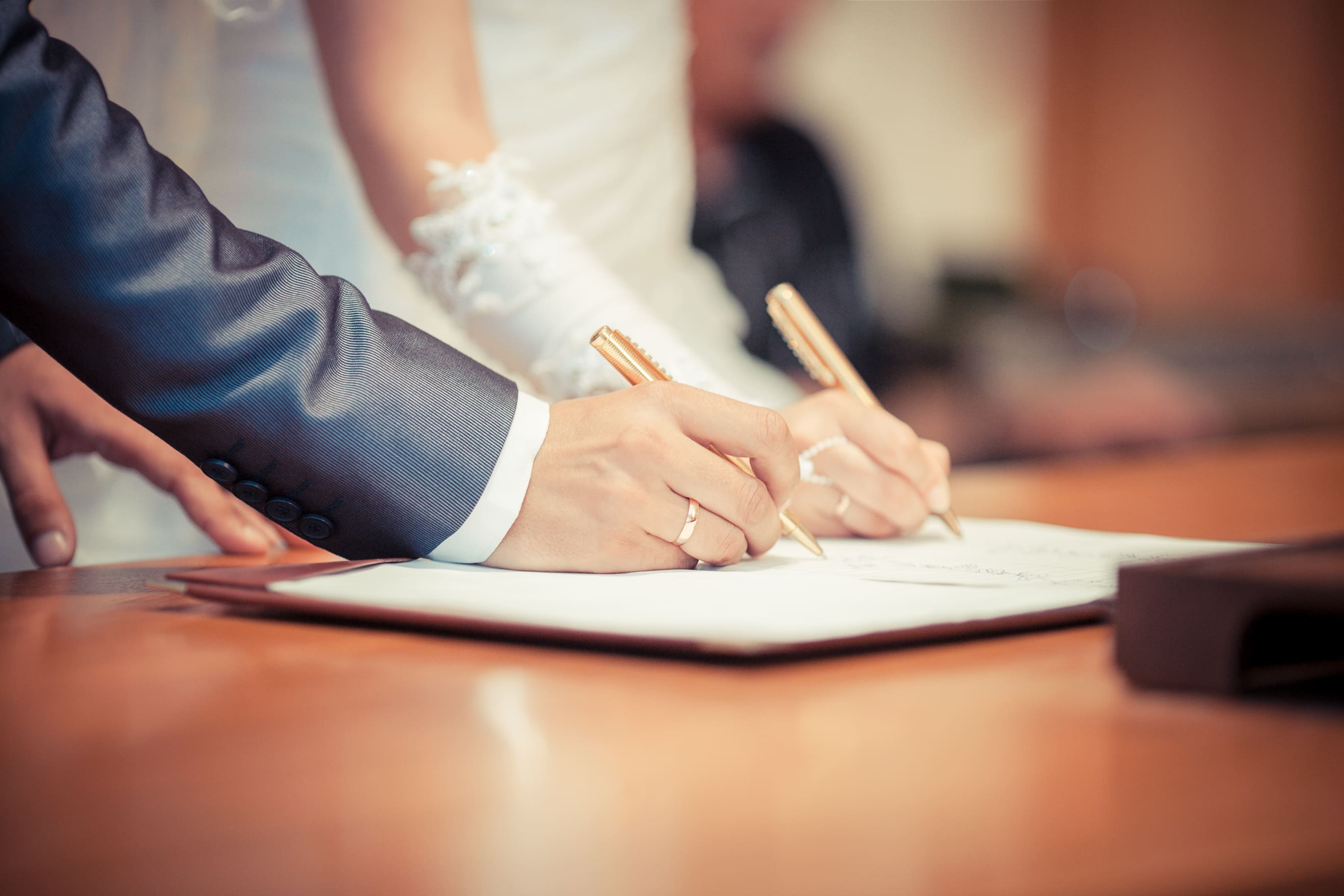Hands of a married couple signing document together.