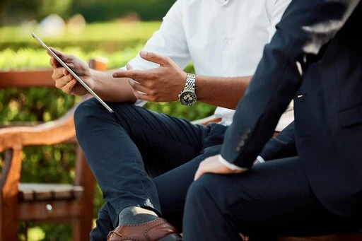 Lower shots of business man seated, with one pointing to tablet screen,.