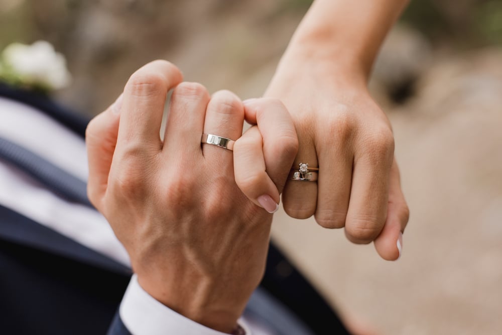 couple interlocking pinky fingers wearing wedding bands