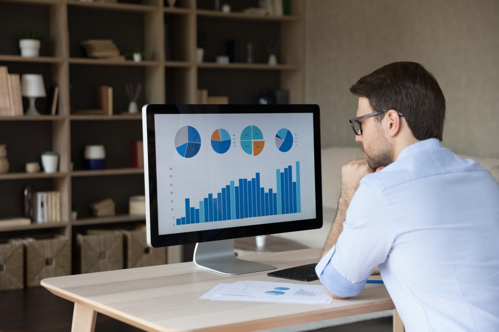 Man looking at computer monitor showing pie charts and bar graphs in home office setting