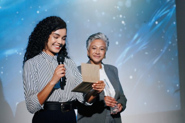 A woman stands with a microphone and a card after accepting an award in the sciences.