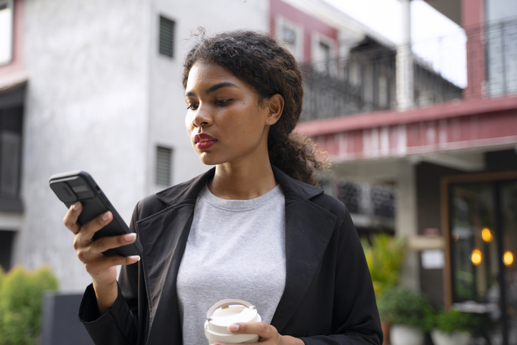 Business woman is outside and looking at her phone anxiously.