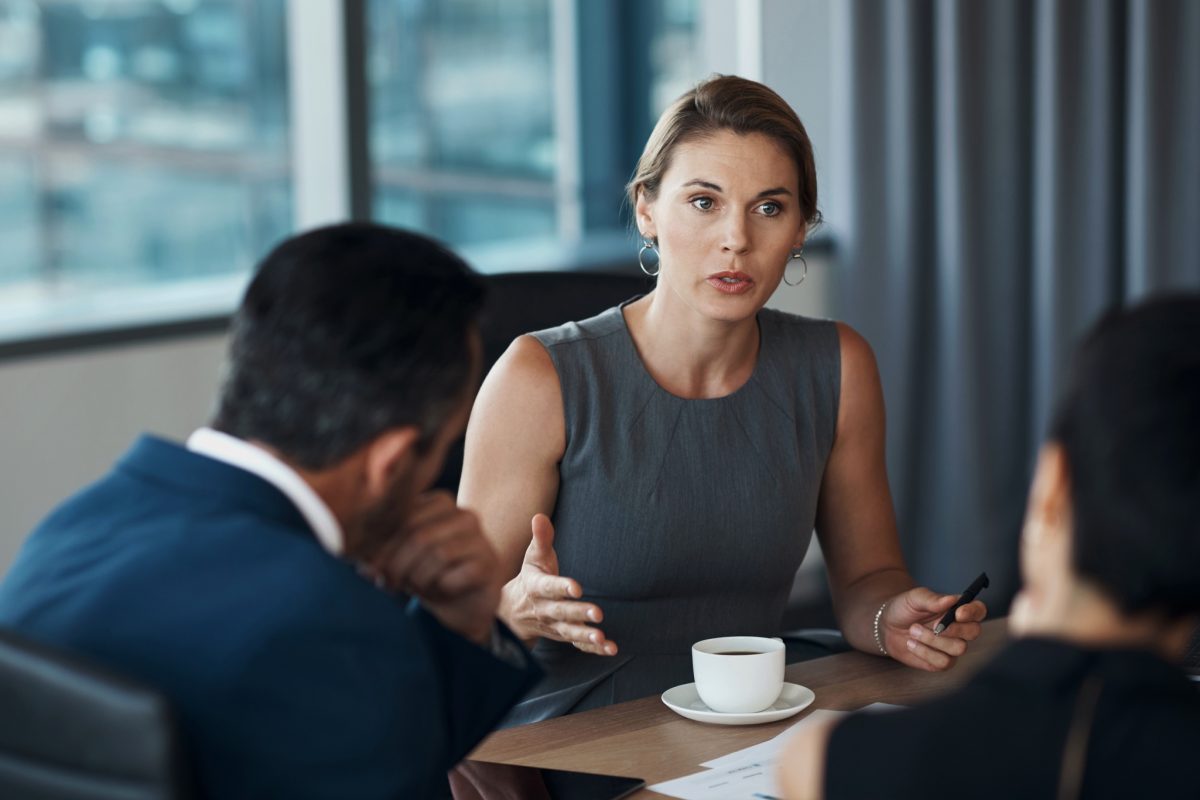 A woman lawyer sits at a desk and talks seriously to multiple clients.