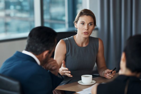 A woman lawyer sits at a desk and talks seriously to multiple clients.