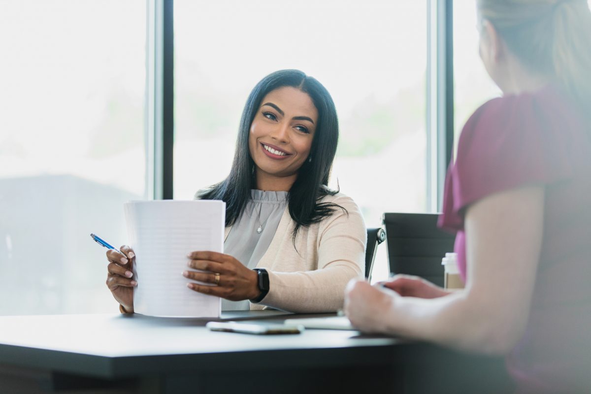 A female boss smiles at her employee while holding an employment verification letter.