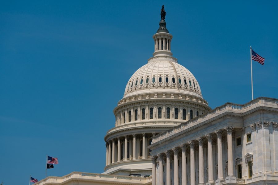 Congress building with blue sky behind it and American flag - government shutdown begins on Oct 1