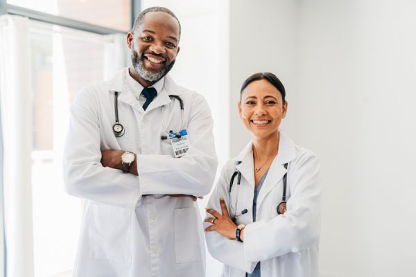 Two doctors stand side by side smiling.
