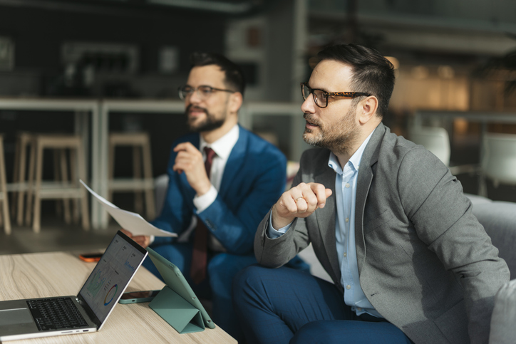 Two businessmen investors are discussing an investing strategy while looking at a laptop and documents.