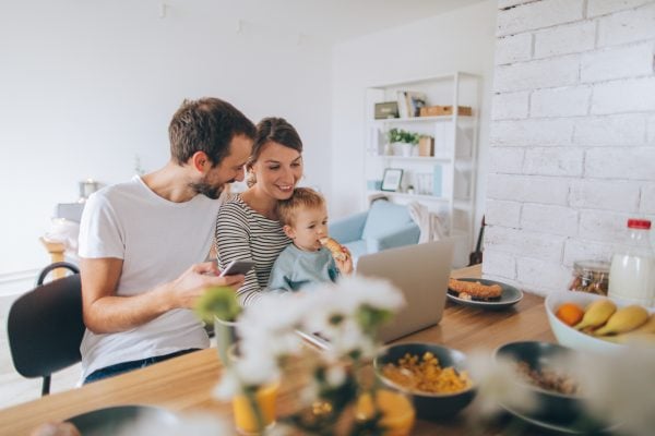 A female F-1 student visa holder is sitting at a table with her husband and young child, while breakfast and an open laptop sits in front of them.
