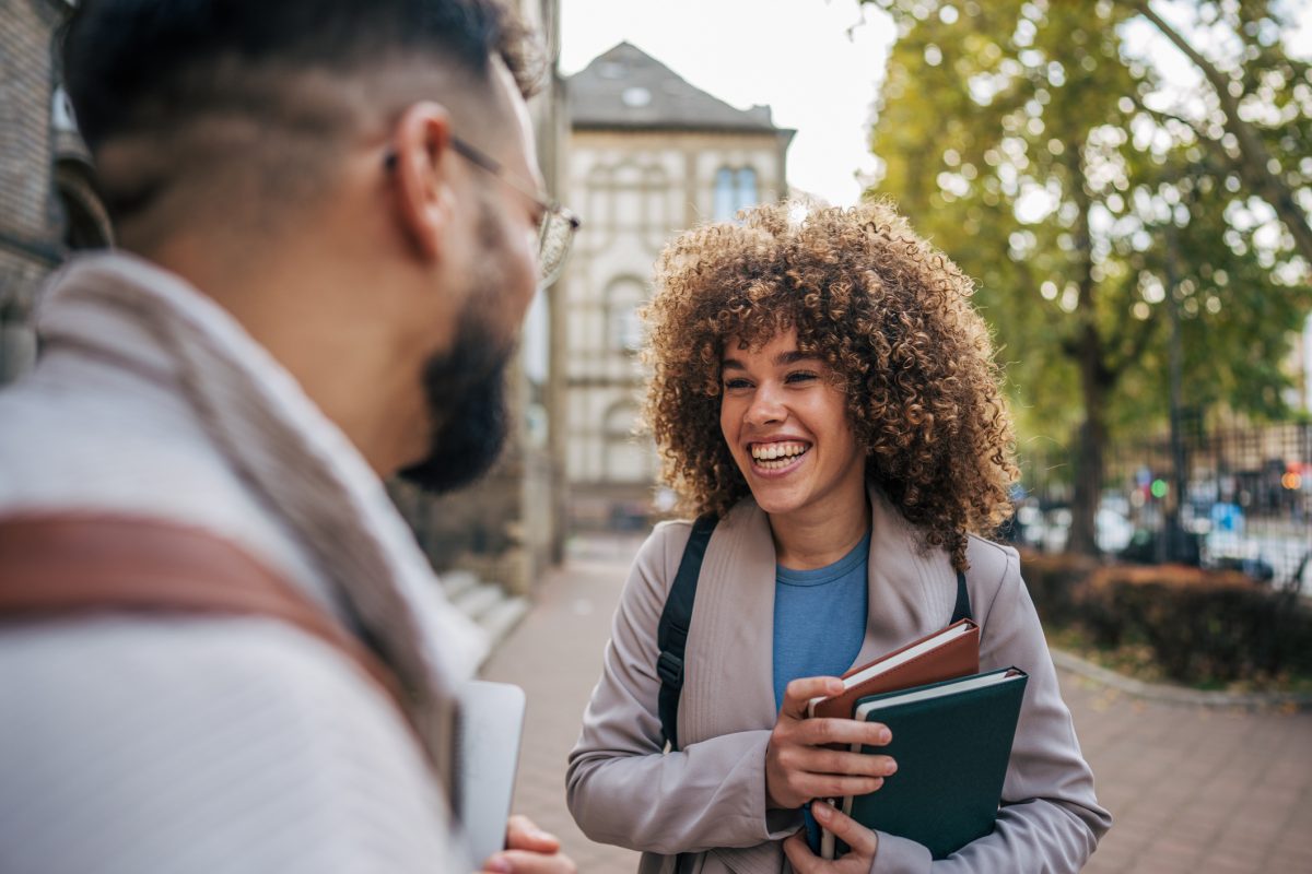 Two students, one male and one female, stand on a university campus smiling after transferring from an H-1B to an F-1 visa.