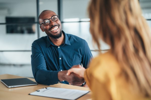 Business workers sit at an office desk shaking hands.