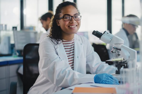 A medical exchange visitor sits in front of a microscope smiling.