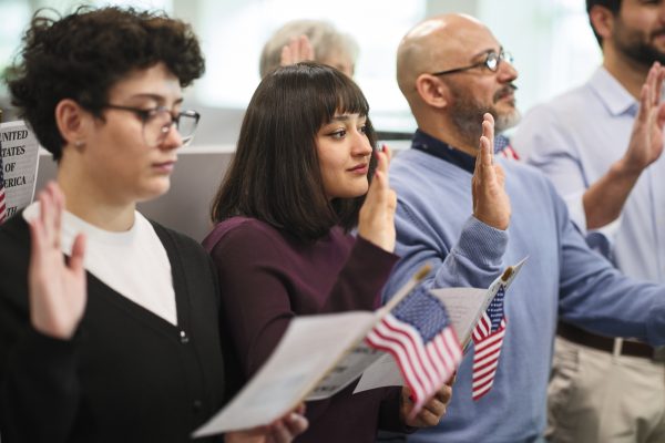 A group of people stands with one hand in the air as they take the Oath of Allegiance to become U.S. citizens.