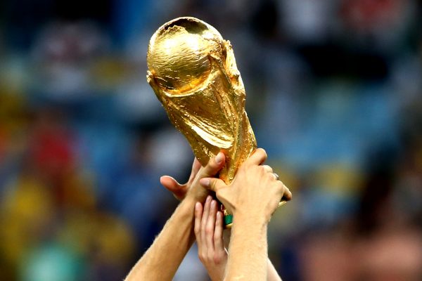 Close-up of World Cup being held up by several people's hands.
