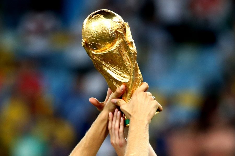 Close-up of World Cup being held up by several people's hands.