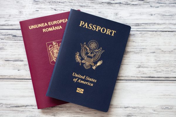 Two passports, one for the U.S. and one for Romania, laying on a white tabletop.