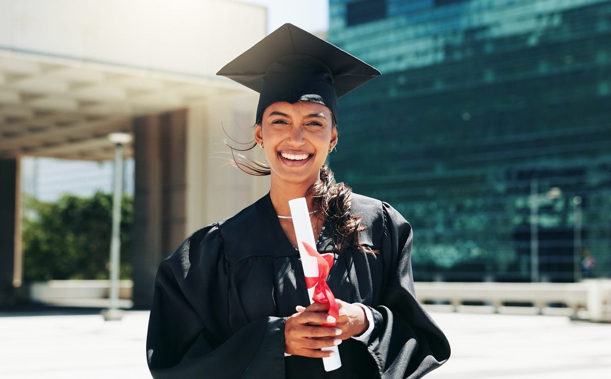 Portrait of a woman wearing graduation cap and gown and holding a diploma.