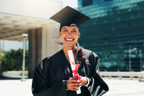 Portrait of a woman wearing graduation cap and gown and holding a diploma.