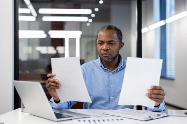 A man sitting at a desk is holding up two documents as he considers his visa options.