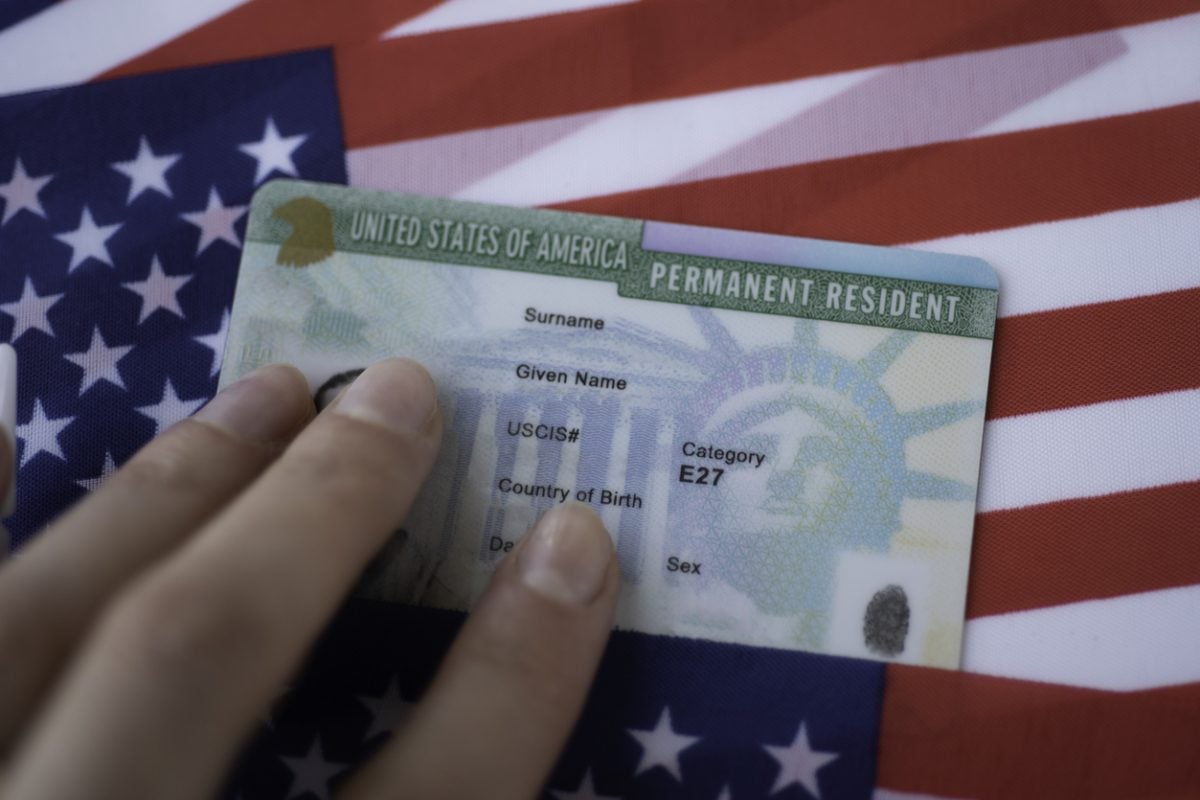 Closeup of Green Card against American flag backdrop.