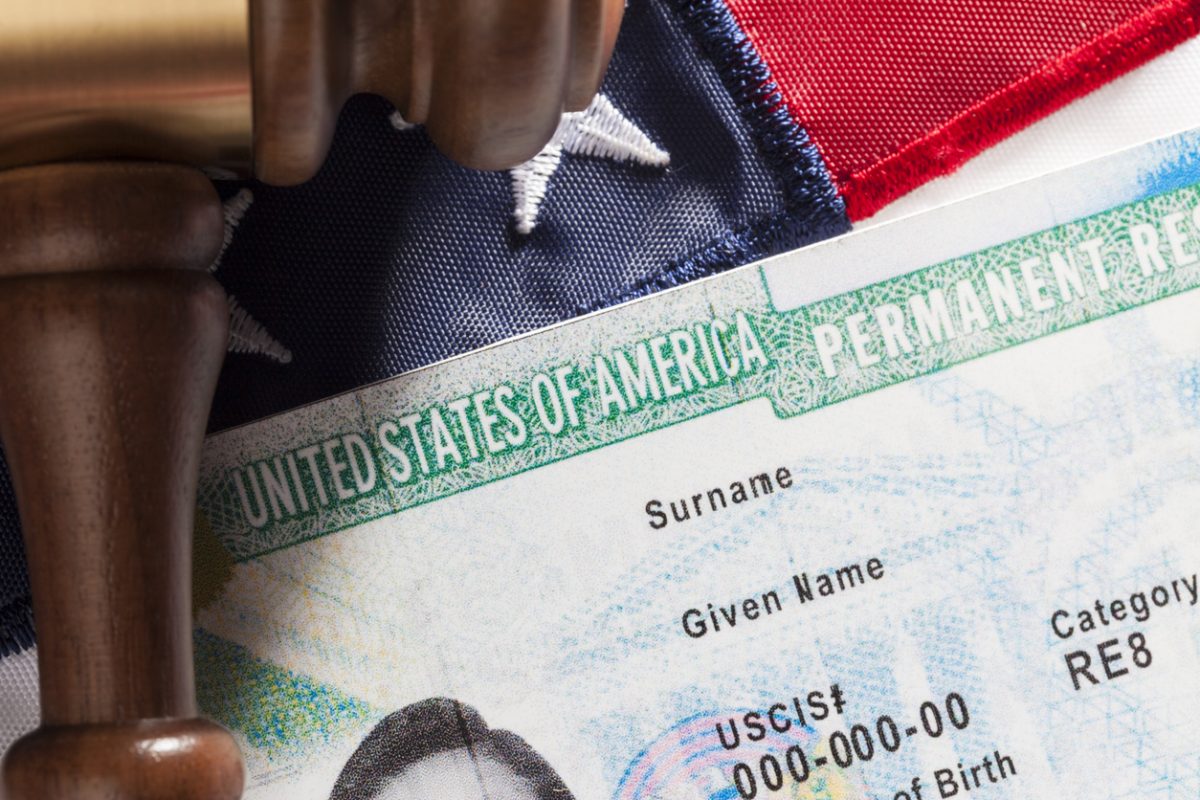 Closeup of a Green Card against an American flag backdrop.