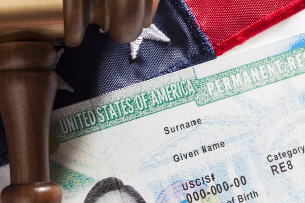 Closeup of a Green Card against an American flag backdrop.