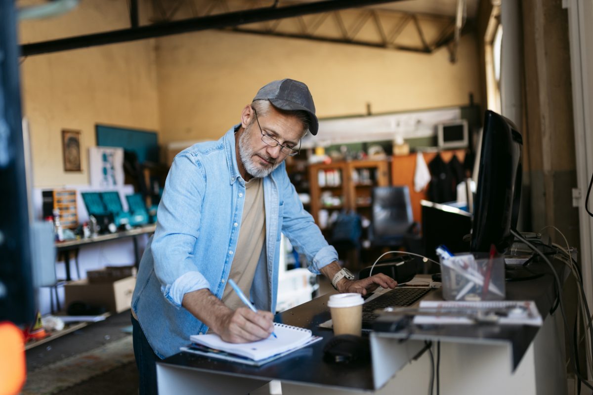 Small business owner working at the front desk of his workshop and taking notes in a notepad.