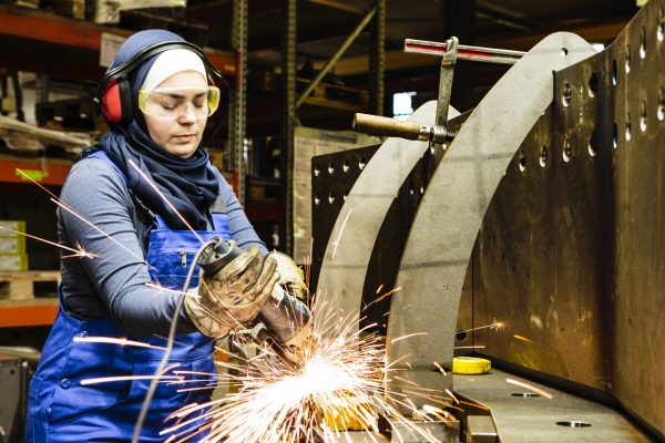 Worker welds steel with a grinder in her workshop.