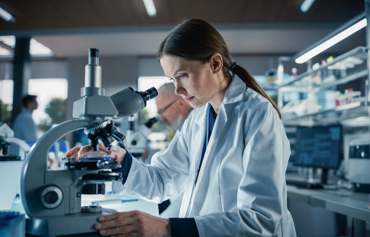 Bioengineer looking at DNA samples under a microscope in her lab.