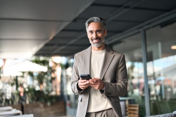 Entrepreneur holding his phone while standing outside and smiling.