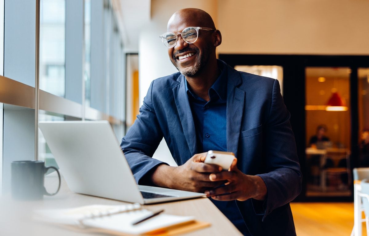 Businessman in office smiling while looking up from his laptop.