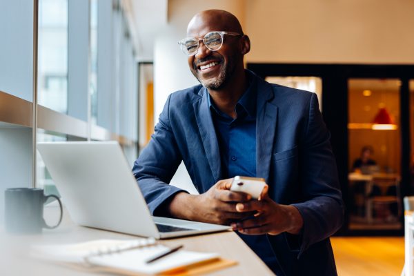 Businessman in office smiling while looking up from his laptop.