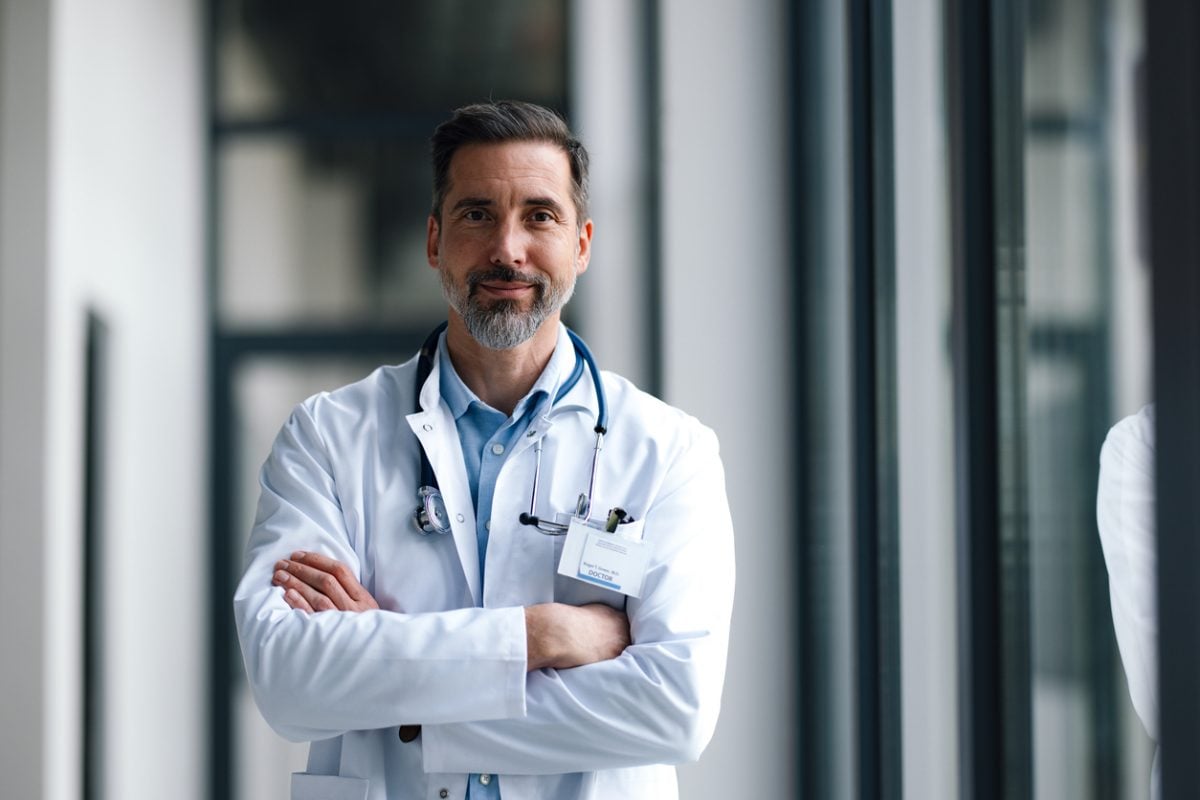 Confident senior doctor standing in office with arms crossed.